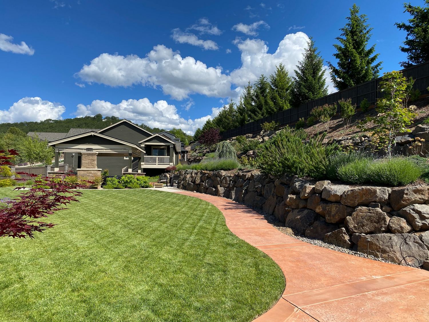 Finished lawn and curved hardscape path across a sloped landscape